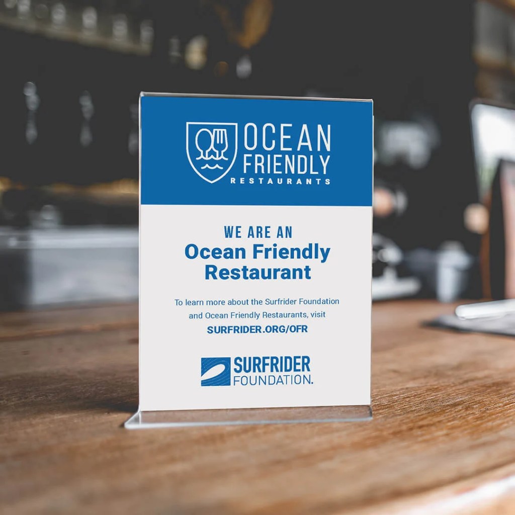 A sign on a table indicating the restaurant is 'Ocean Friendly' and affiliated with the Surfrider Foundation, promoting sustainability in dining.